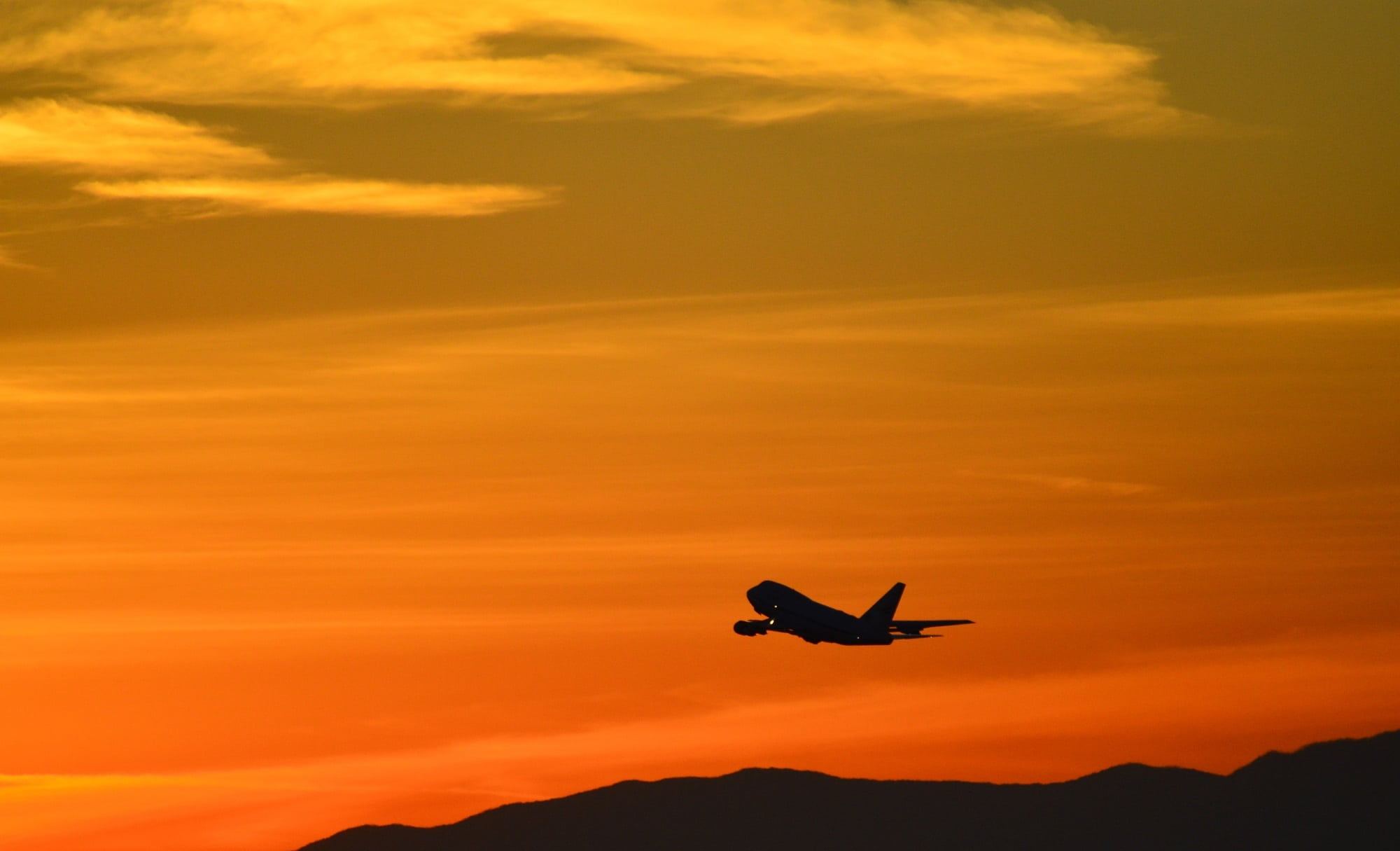 A four-engine jet climbing out against an orange sunset sky